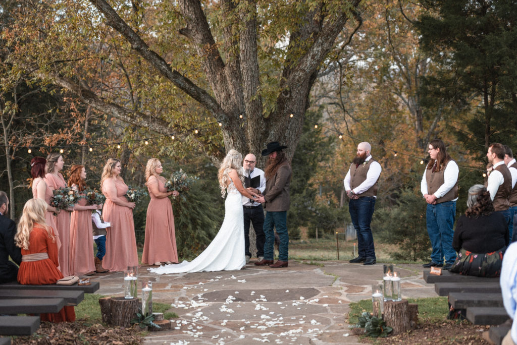 Bride and groom say I do in front of large oak tree during outdoor ceremony at the barn at high point farms.