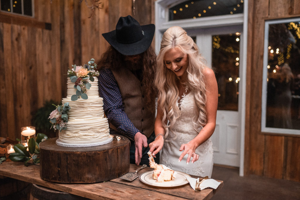 Bride and groom cut the wedding cake in reception hall at the barn at high point