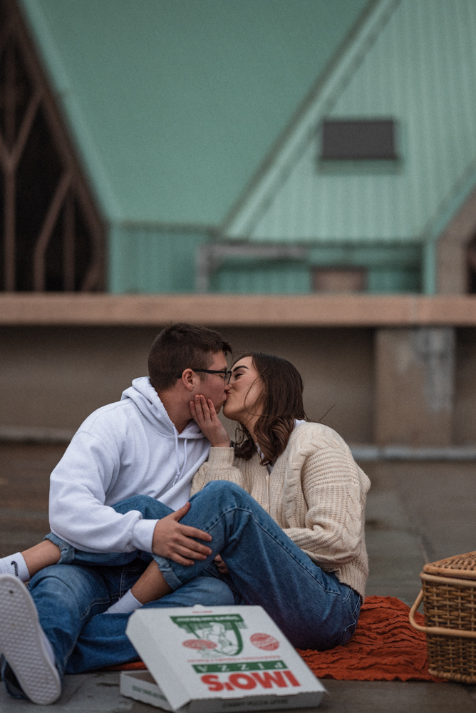 Couple takes a break from enjoying imo's pizza on the rooftop picnic to steal a kiss in st louis mo