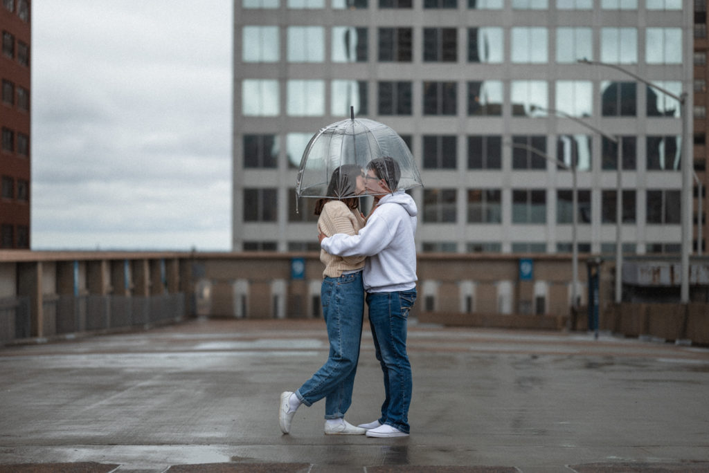 Who needs two umbrellas when your love will share. Adorable couple kisses under clear umbrella on st louis rooftop during date night