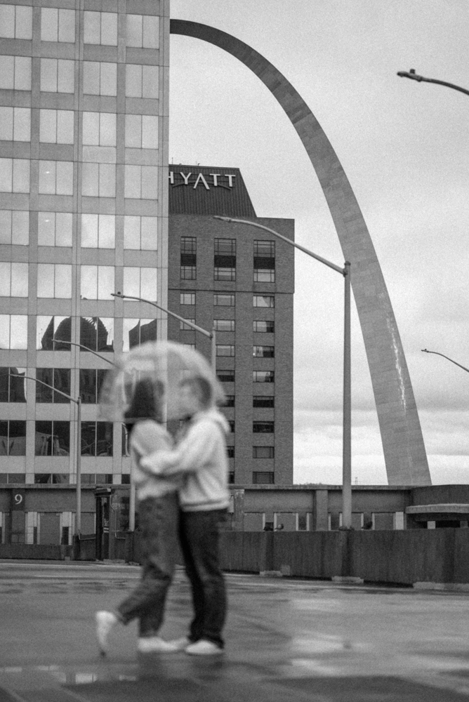 St louis gateway arch is seen clearly as couple embraces under clear umbrella during date night