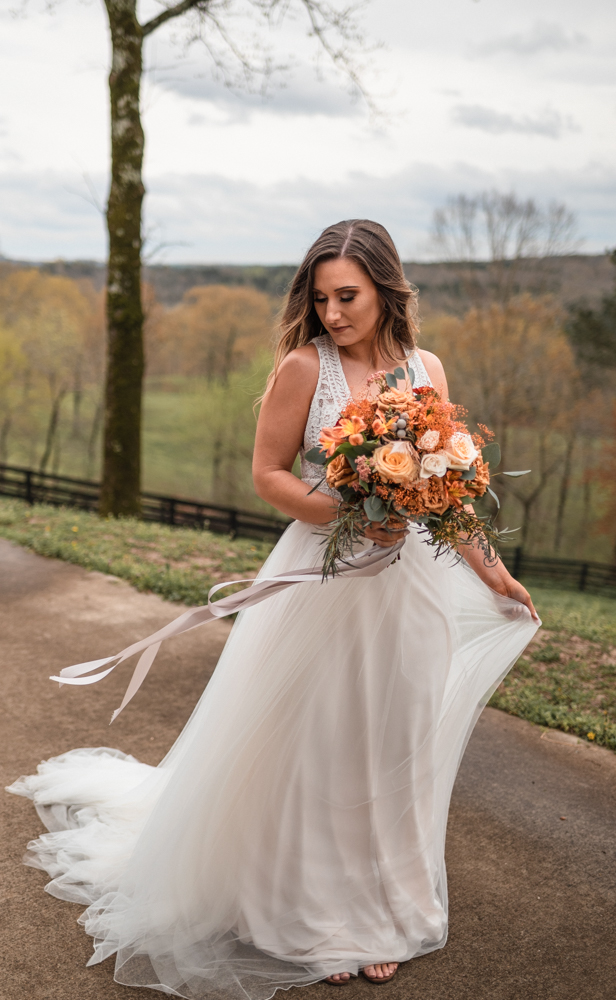 Boho bride gazes down as she stands in front of the georgia mountains with a bouquet from arrangements by rachel