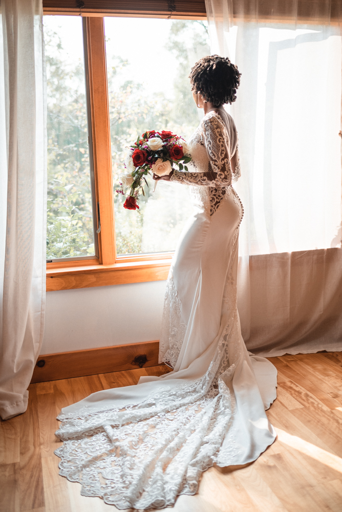 Bride gazes out window in her wedding dress in some of her last moments before becoming a Mrs.