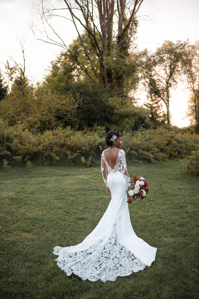 Beautiful bride stands elegantly in lace wedding gown in a field of wild flowers.