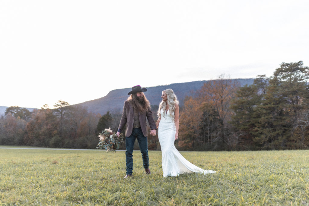 The newly wedding boho couple walks hand in hand in front of mountains