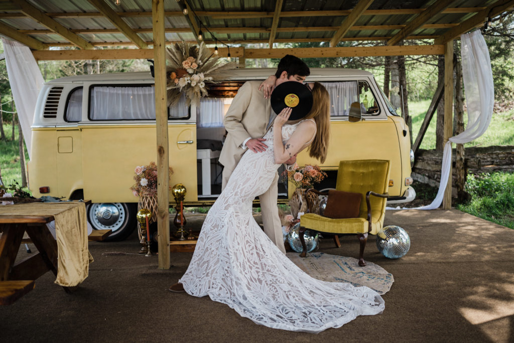 The vw bus and boho scene is hidden by the sweet boho couple's kiss at the adorable glamping site.