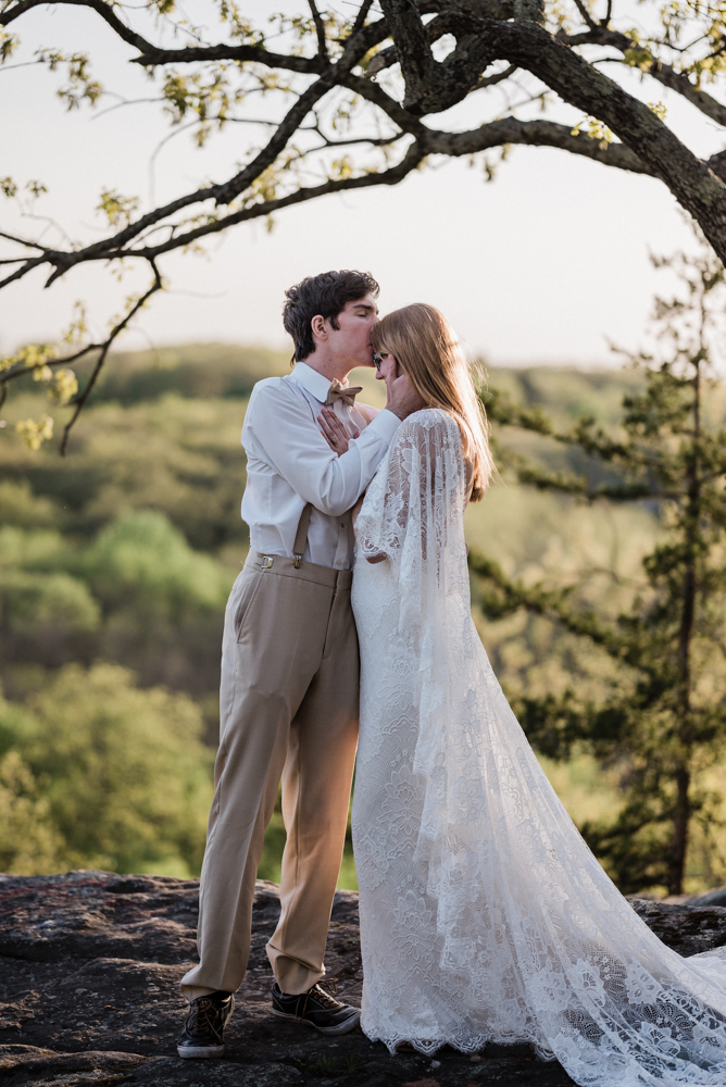 The young boho elopement couple shares a kiss on thinking rock over the Meramec River not far from Jefferson city, MO