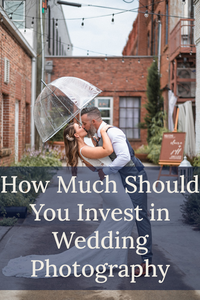 Wedding on rainy day Couple has clear umbrella and groom passionately dips and kisses bride in tight lace dress in urban alley with red bricks and green landscaping