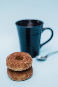 2 gluten free vegan cinnamon sugar donuts stacked near blue coffee mug on light blue backdrop