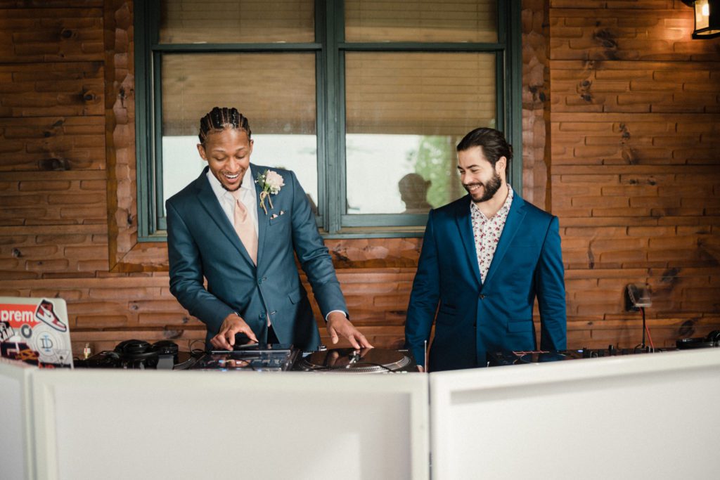 Groomsman takes over the dj booth and shows his skills to a wedding guest before the reception begins at the five star lodge and stables in Morganton, GA.