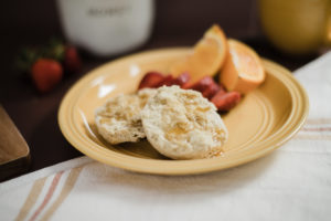 Sage Vegan Breakfast biscuits on yellow plate drizzled with all natural honey from Sammons Bee Farms in New Melle Mo laid next to Hearth and Hand white and orange dish towel