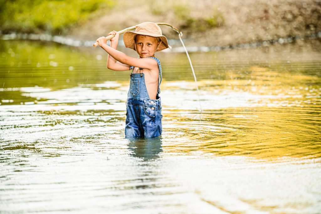 Young blonde boy with blue concentrates before casting his line into the creek for st charles family portraits.