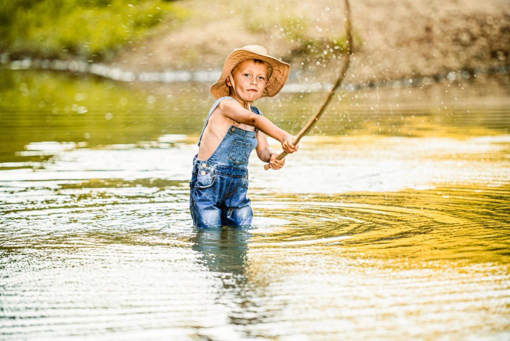 Young boy casts his fishing line with great concentration and allows water to splash all around him.