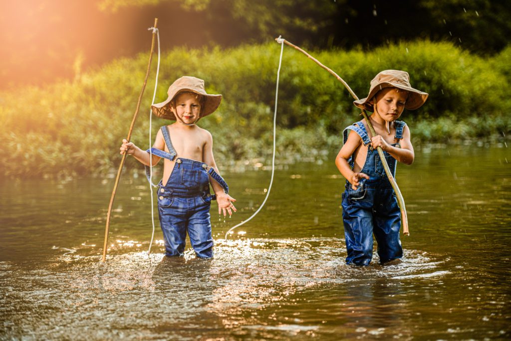 Two young children carry their fishing poles while wearing blue jean overalls and hats gearing up to splash water from this cottleville, Mo creek during their unique family photography session.