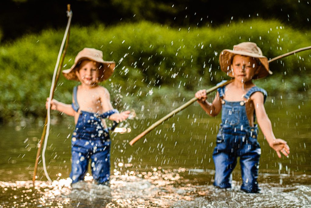 Water splashes towards the camera in Lake St Louis, MO family photography session with two young boys dressed to go fishing in the creek.