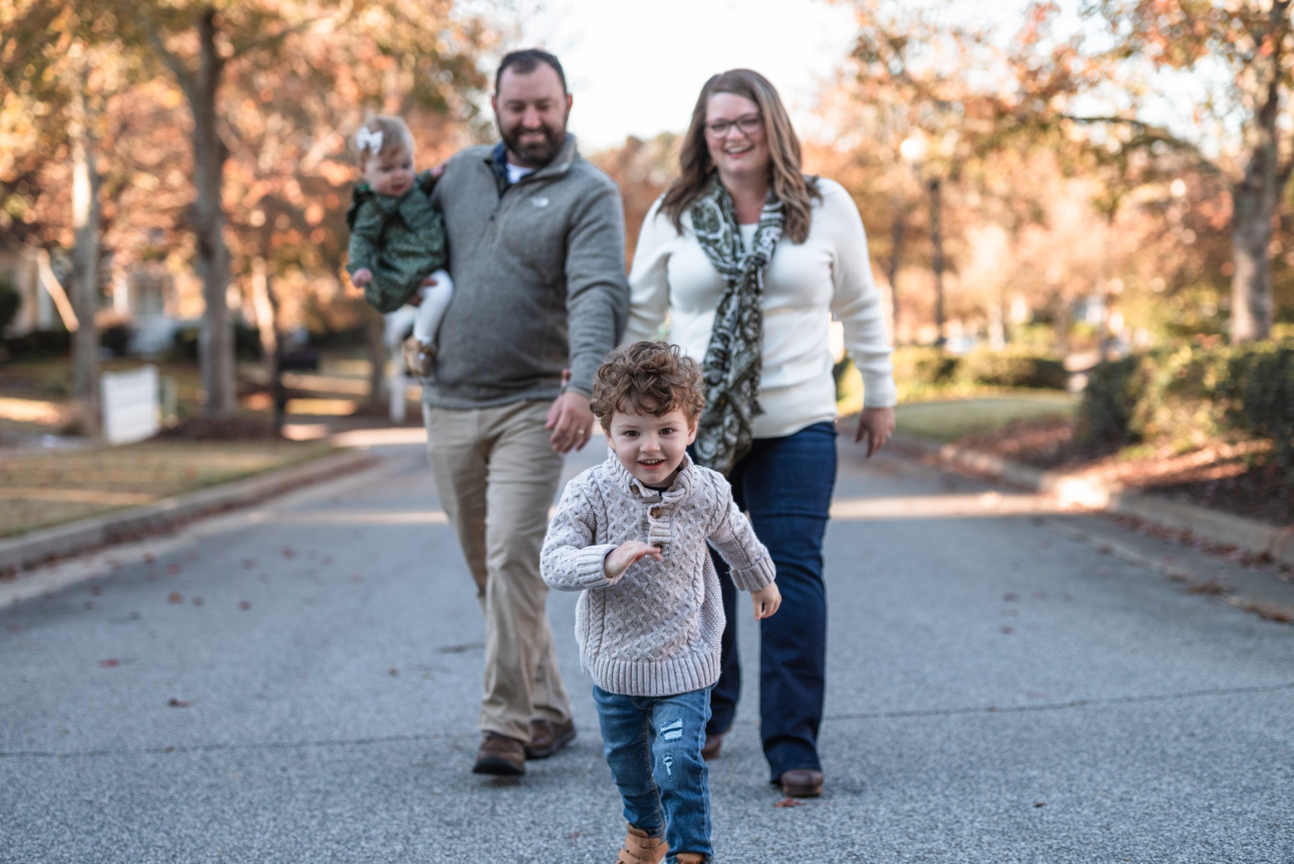 Toddler boy running towards camera while parents smile and laugh during st louis family photography session