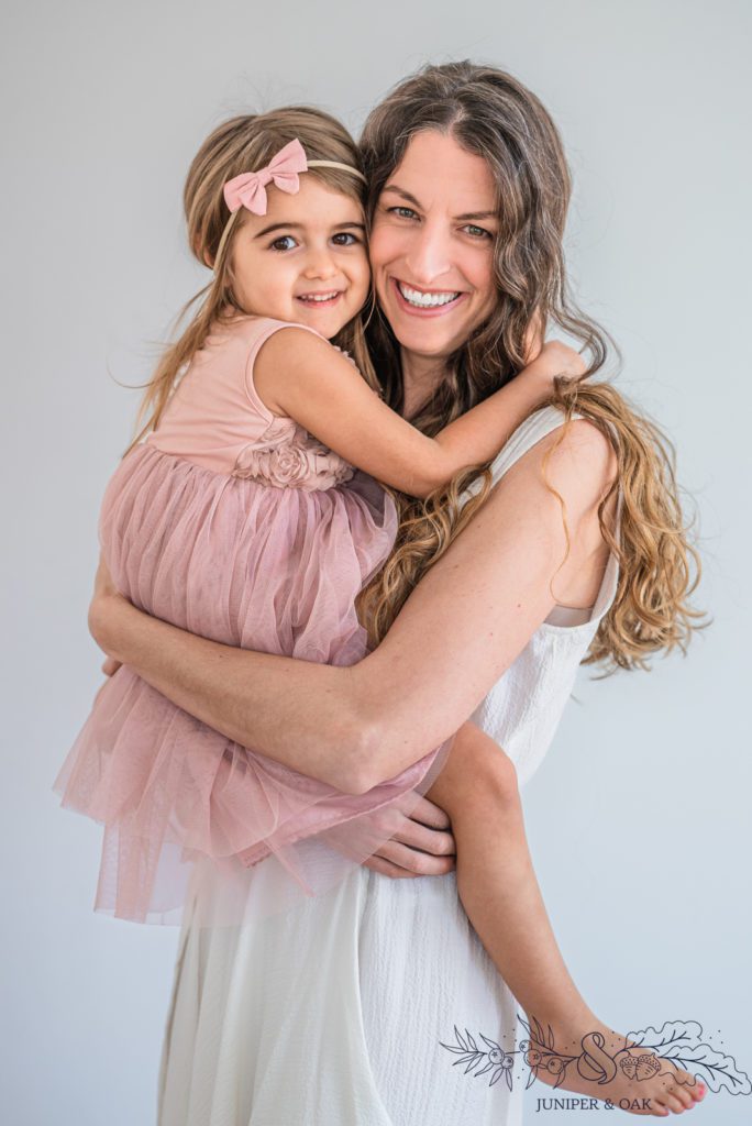 Mom and daughter taking a photo wearing pastel colors with a white background and natural light taken by st louis family photographer Juniper & oak photo