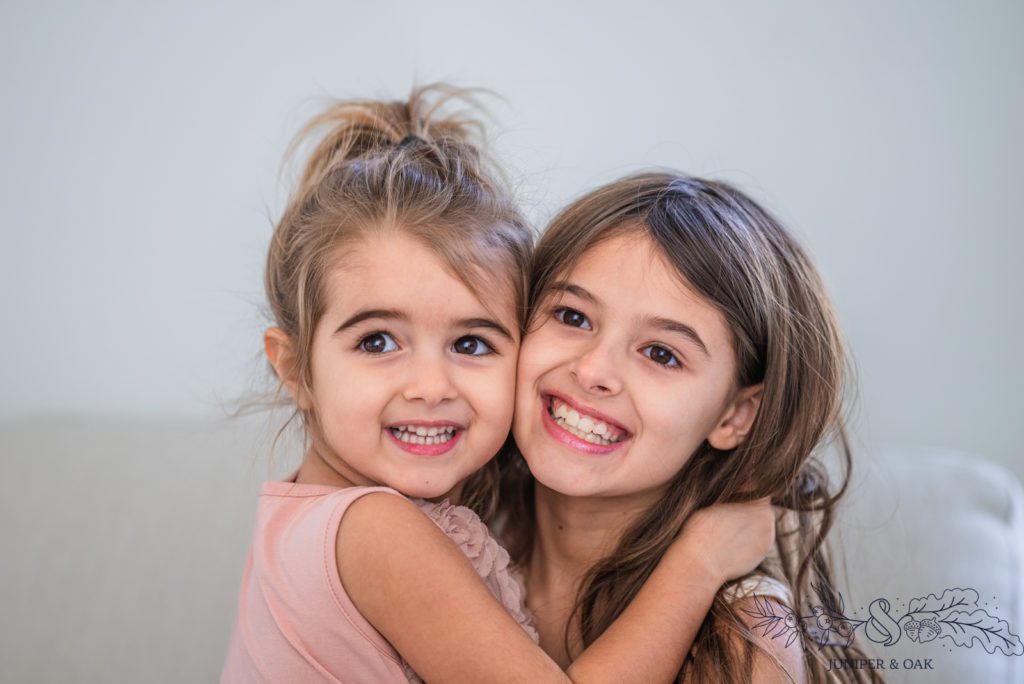 Two young brown eye sisters hug each.