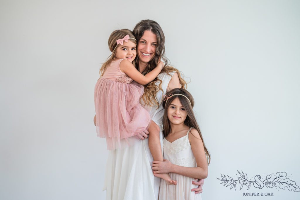 Motherhood photo with mom and two young daughters with a white background in studio in downtown st charles.